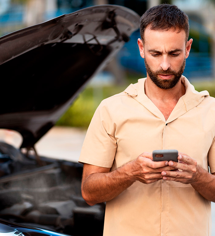 Persona escribiendo por WhatsApp junto a su auto con el capó abierto